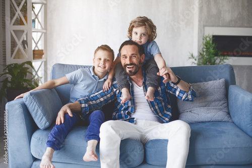 Portrait of cheerful father having fun with two outgoing children while sitting on sofa. Glad parent with positive sons concept