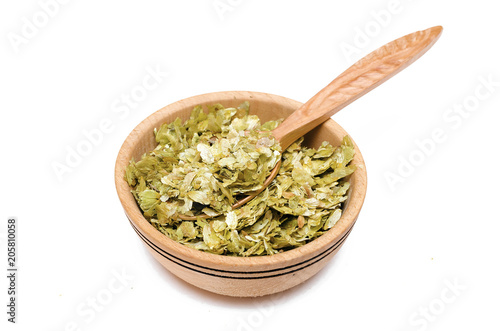 Granulated green hop leaves in the wooden bowl with wood spoon isolated on white background.