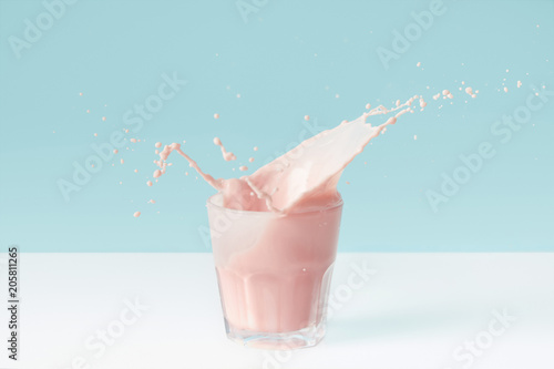splashing drops of strawberry milkshake from glass on blue background