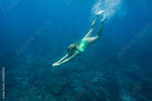 underwater photo of young woman in swimming suit diving in ocean alone