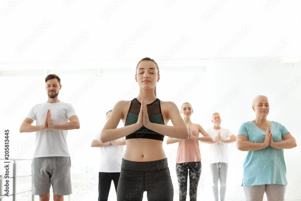 Naklejka premium Group of people in sportswear practicing yoga indoors