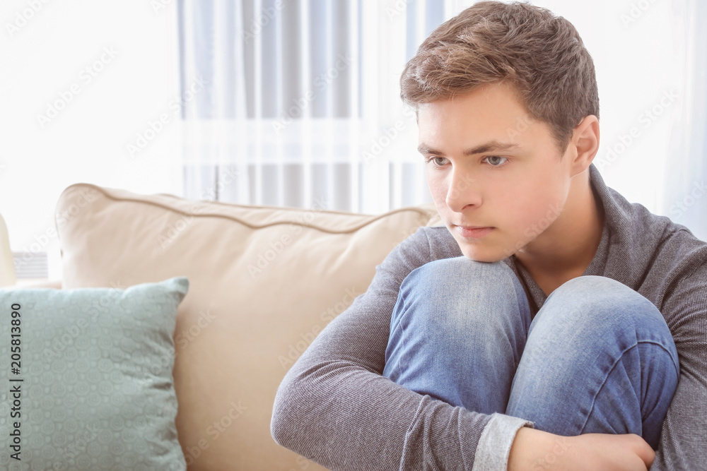 Depressed teenager sitting on sofa in room Depressed teenager sitting on sofa in room