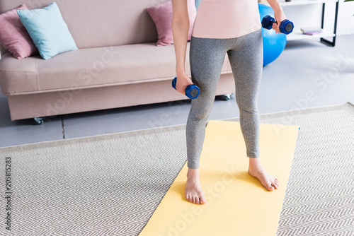 cropped shot of woman standing on yoga mat with dumbbells at home