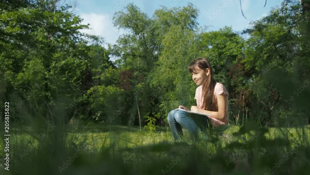 A child draws in nature. Little girl draws with a pencil in the park A child draws in nature. Little girl draws with a pencil in the park