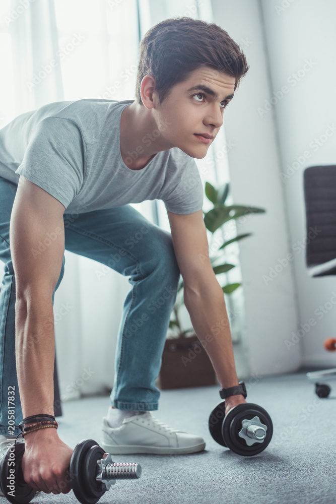 handsome teenager squatting with dumbbells at home handsome teenager squatting with dumbbells at home