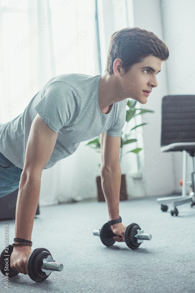 handsome teenager doing push ups with dumbbells at home