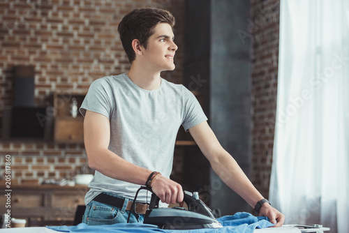 dreamy caucasian teenager ironing blue shirt at home
