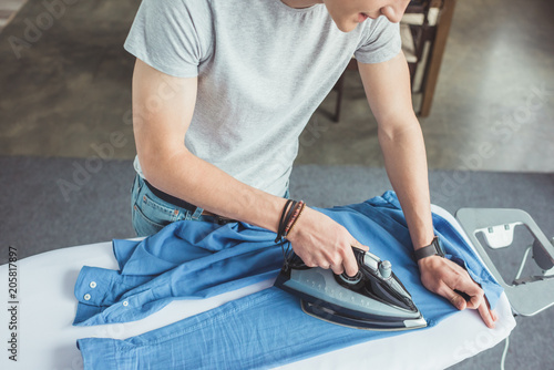 cropped view of teenager ironing blue shirt with iron at home