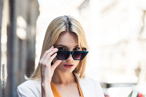 portrait of beautiful young blonde woman adjusting sunglasses and looking at camera