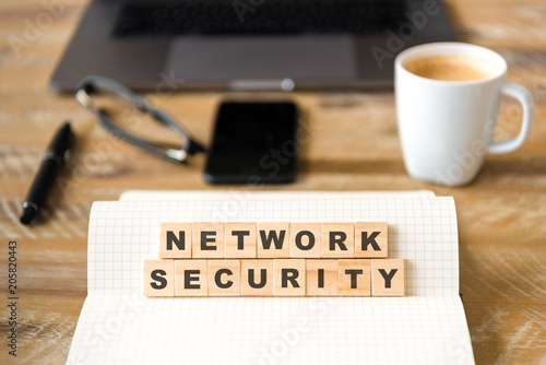 Closeup on notebook over wood table background, focus on wooden blocks with letters making NETWORK SECURITY text