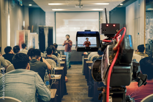Closeup Video recording the Asian Speaker with casual suit on the stage over the presentation screen in the meeting room of business or education seminar, event and seminar concept