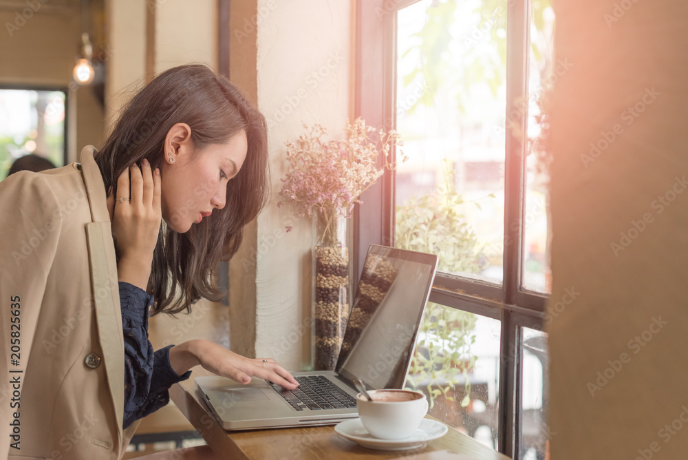 Young businesswoman sitting in coffee shop at table in front of laptop and drinking coffee. On background white brick wall and window. Girl shopping online, blogging, checking email.Online education. Young businesswoman sitting in coffee shop at table in front of laptop and drinking coffee. On background white brick wall and window. Girl shopping online, blogging, checking email.Online education.