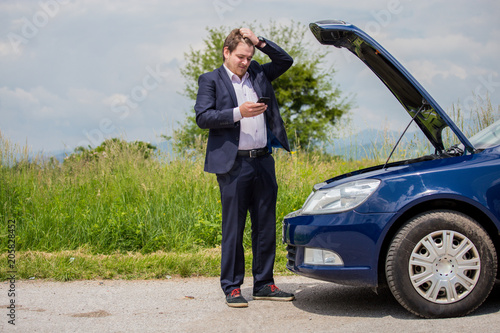 A broken car on the road, the driver is holding his head, an open hood, a car in failure