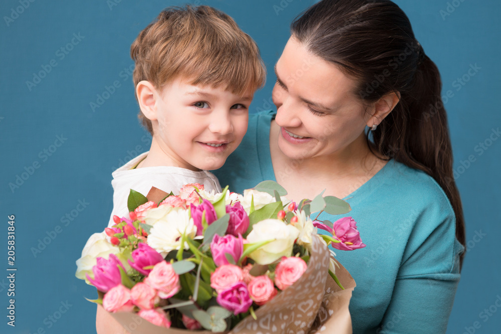 Cute little child hugging and kissing her mother and offering flowers on a blue background. Mother's day, birthday Cute little child hugging and kissing her mother and offering flowers on a blue background. Mother's day, birthday