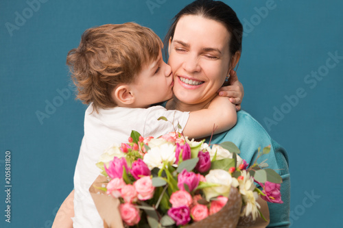 Cute little child  hugging and kissing her mother and offering flowers on a blue background. Mother's day, birthday