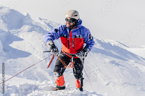 Happy climber with an alpinism shell goes up the ice to the top. Mountaineer with equipment on the glacier.