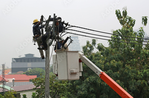 Electricians resting while working to replace the electrical insulator on the electricity pole.