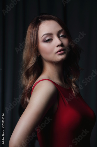 Charming brunette in a red dress posing on a black background. © ASDF