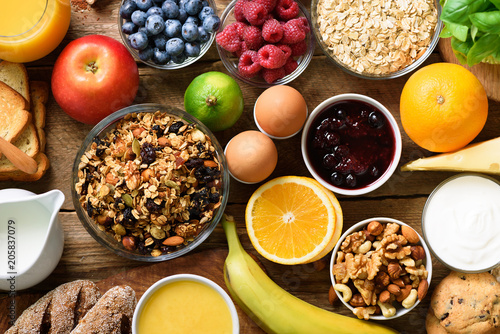Healthy breakfast ingredients, food frame. Granola, egg, nuts, fruits, berries, toast, milk, yogurt, orange juice, cheese, banana, apple on wooden rustic background, top view, copy space.
