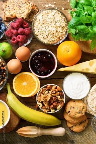 Healthy breakfast ingredients, food frame. Granola, egg, nuts, fruits, berries, toast, milk, yogurt, orange juice, cheese, banana, apple on wooden rustic background, top view, copy space.