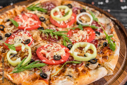 Vegetables, mushrooms and tomatoes pizza on a black wooden background. It can be used as a background