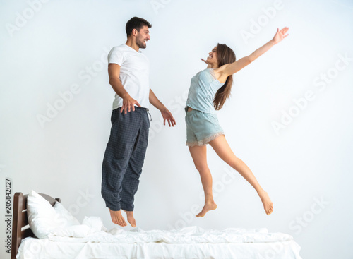 The happy man and a woman jumping on the bed on the white background