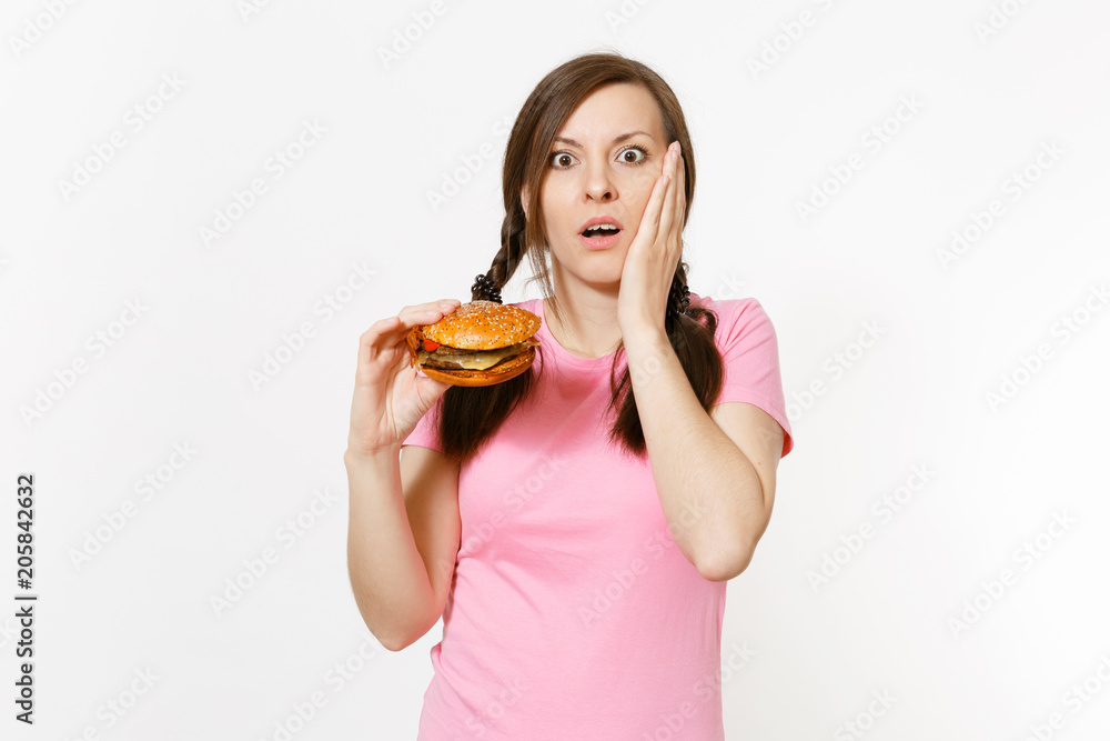 Young beautiful woman in pink t-shirt with braids holding in hands burger isolated on white background. Proper nutrition or American classic fast food. Copy space for advertisement. Advertising area. Young beautiful woman in pink t-shirt with braids holding in hands burger isolated on white background. Proper nutrition or American classic fast food. Copy space for advertisement. Advertising area.
