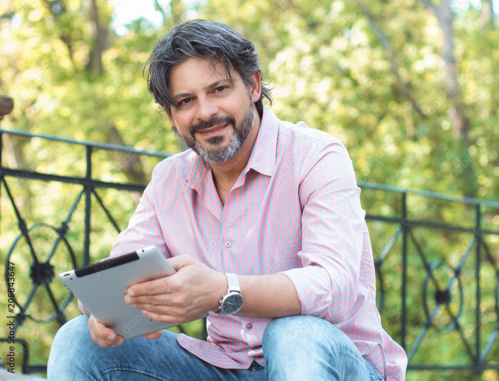 Obraz premium Happy adult handsome man sitting outdoors and tablet