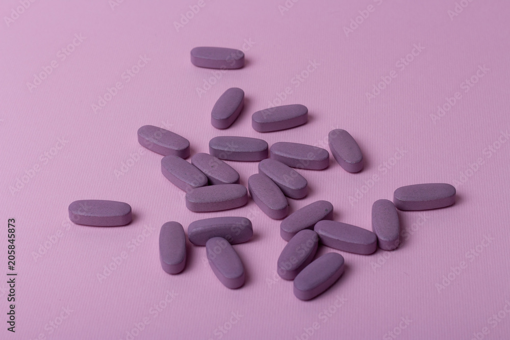 A handful of oval, purple tablets lie on a pink background. A handful of oval, purple tablets lie on a pink background.