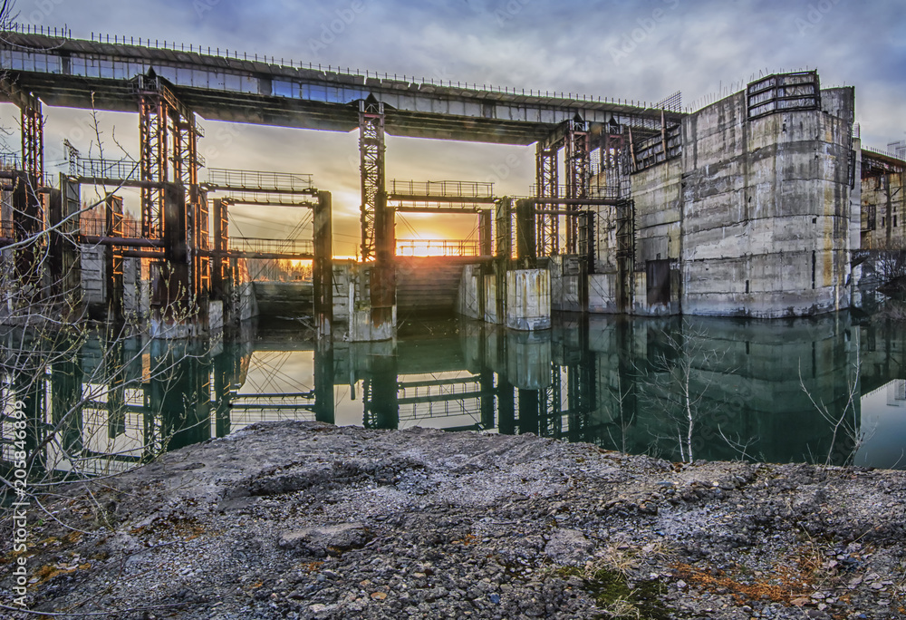 Huge abandoned industrial building on the river damaged hydroelectric sunset view