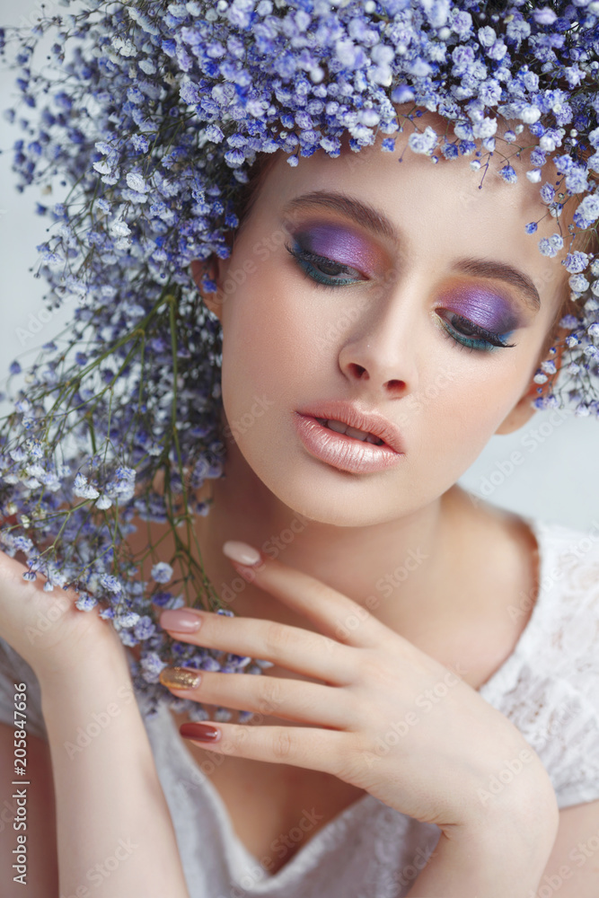 Fashion beauty portrait of a beautiful girl in a voluminous wreath made of small blue flowers on a light background.