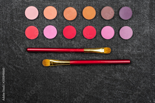 set of matt multicolored circle shaped eye shadows with two brushes laying near. black background and free space for text