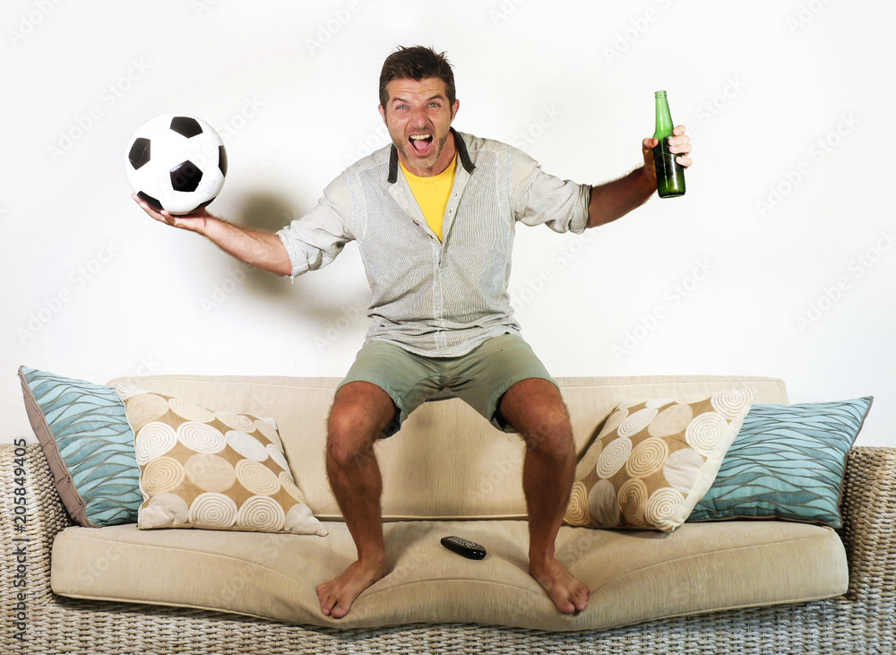 young enthusiastic football fan celebrating goal crazy happy jumping on sofa  couch at home watching soccer game on television holding beer bottle Stock  Photo | Adobe Stock