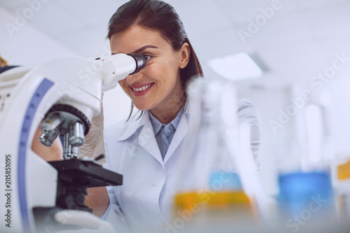 Good mood. Alert professional biologist wearing a uniform and looking into the microscope