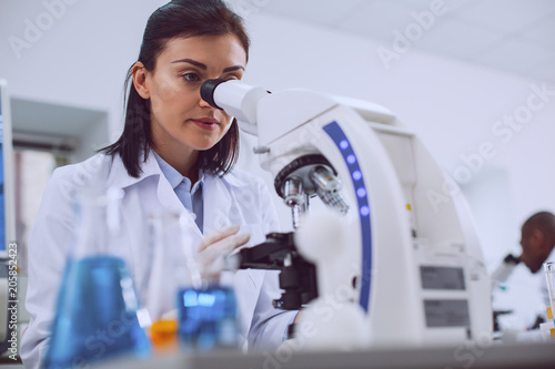 Challenging research. Determined experienced scientist working with her microscope and wearing a uniform