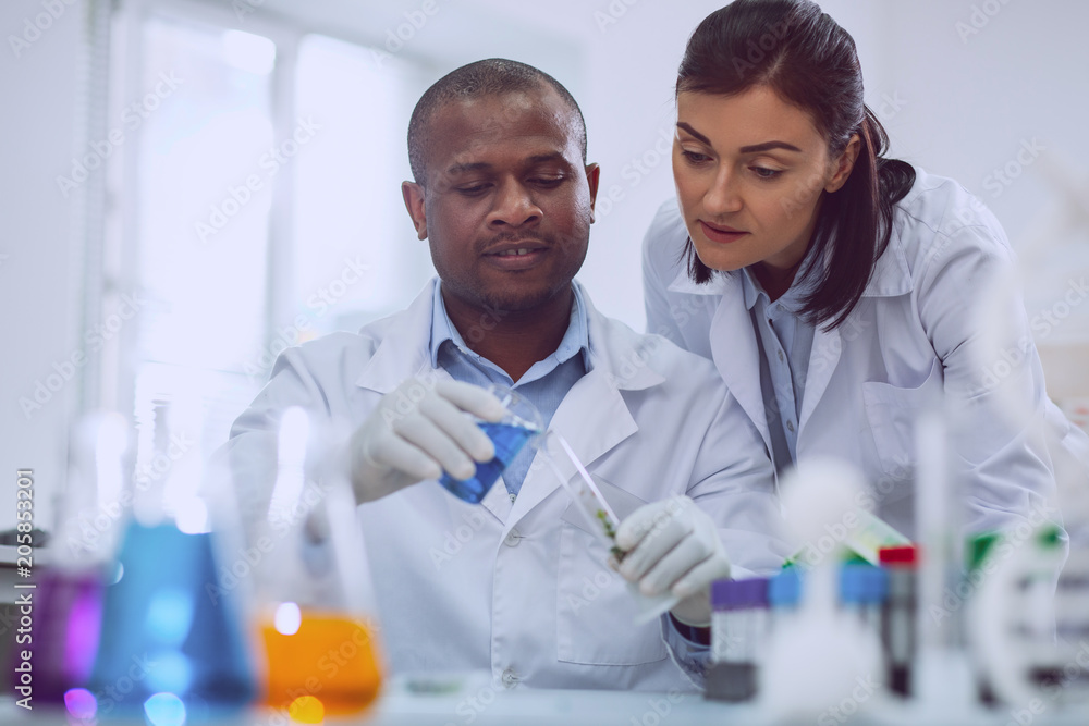 Our new research. Inspired afro-american scientist doing a test and his colleague standing near him Our new research. Inspired afro-american scientist doing a test and his colleague standing near him