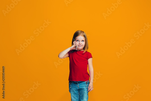 The happy teen girl standing and smiling against orange background.