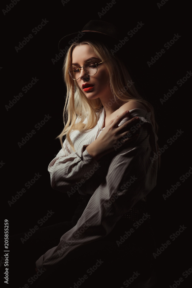 Lovely blonde woman in glasses and hat, posing with dramatic light at studio