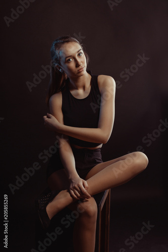 Studio photo session for a young pretty girl posing in the shadows, wearing black apparel
