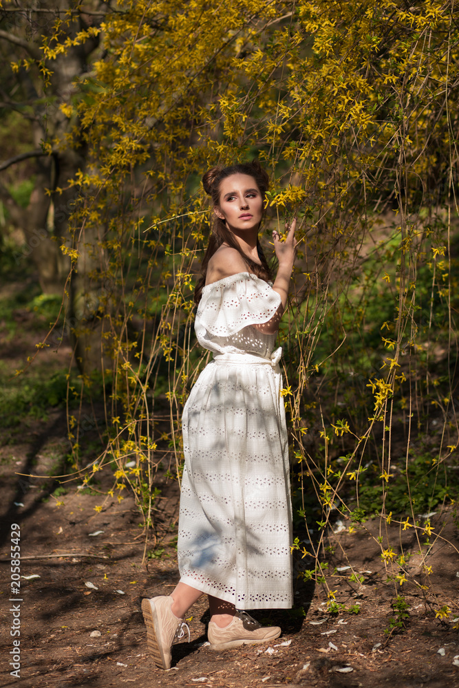 Attractive brunette model posing near the flowering tree in white lace dress