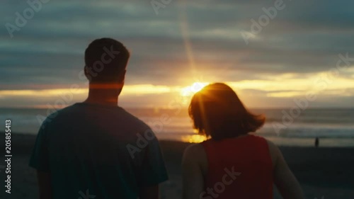Slow motion couple walking on beach at sunset with anamorphic flares photo
