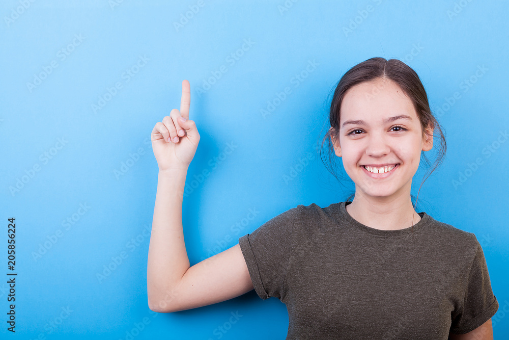 Happy smiling teenage girl pointing up on blue background Happy smiling teenage girl pointing up on blue background
