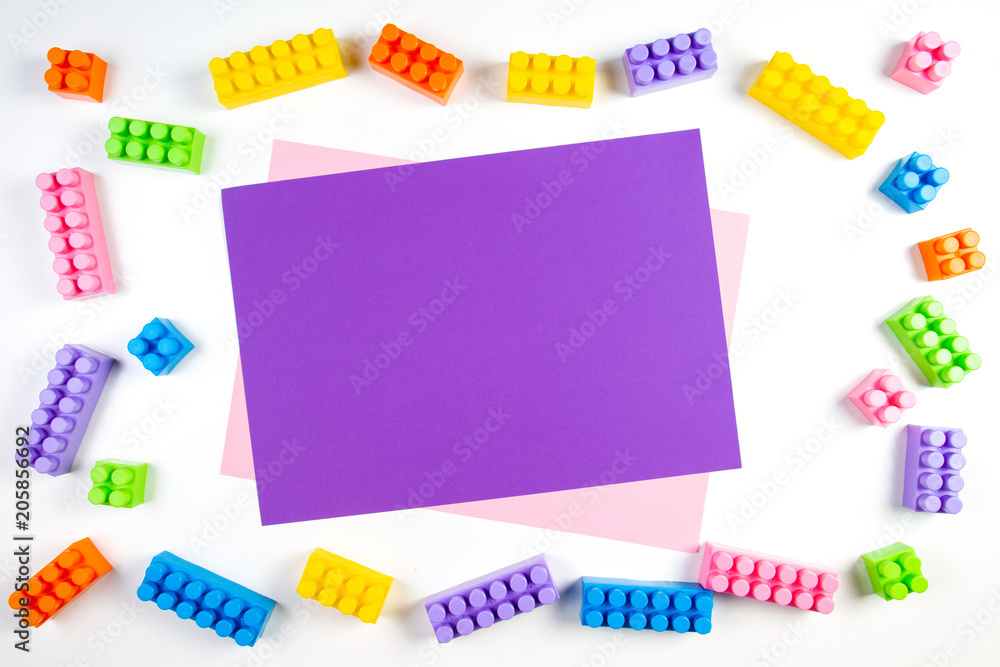 Colorful plastic construction blocks frame with violet blank card on white background Colorful plastic construction blocks frame with violet blank card on white background