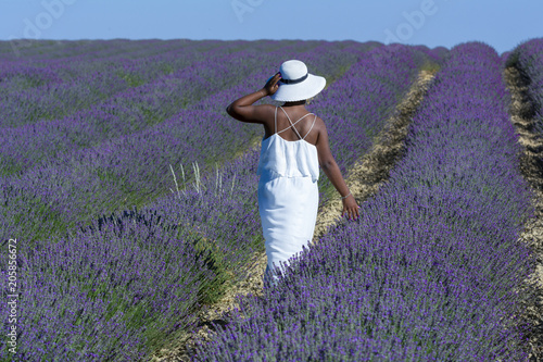 Mujer afroamericana con vestido blanco y sombrero paseando entre las filas de lavanda en flor