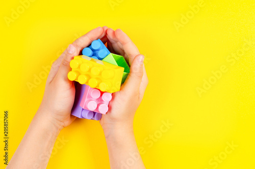 Kids hands hold colorful plastic construction blocks on yellow background