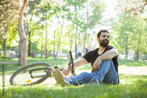 Bearded man next to his bicycle resting on the ground in the park