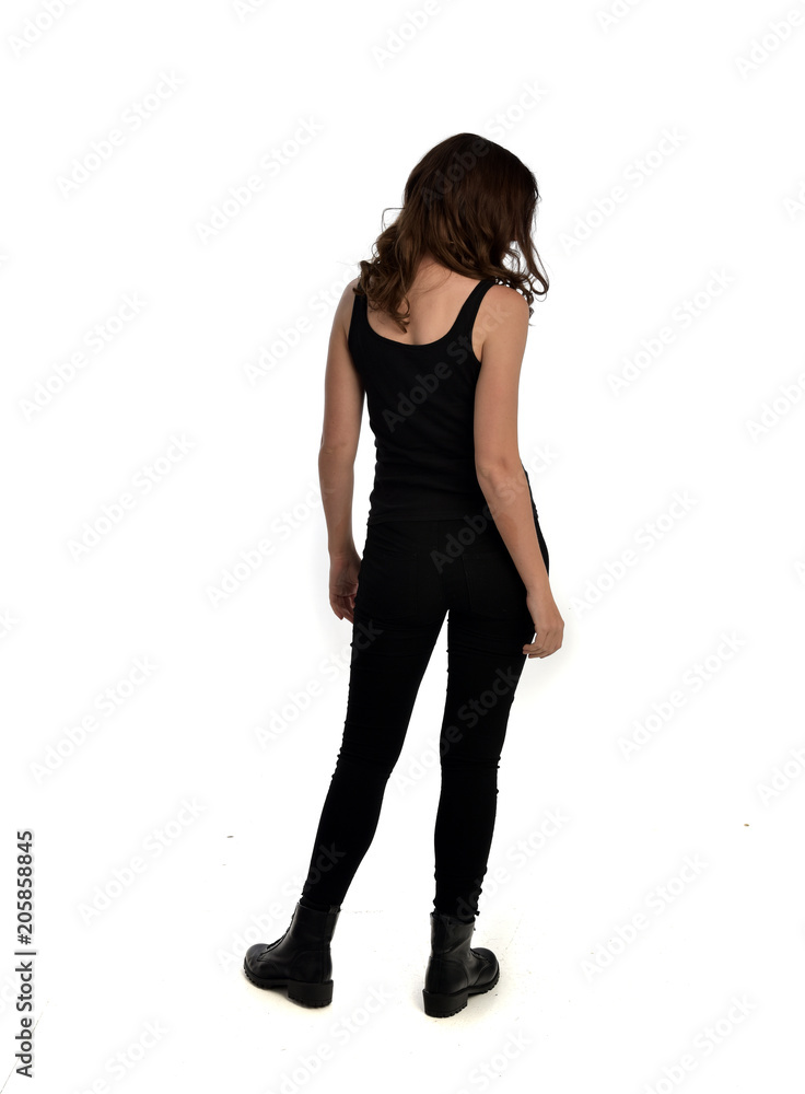 full length portrait of brunette girl wearing black singlet, jeans jeans and boots. standing pose, with back view. isolated on white studio background. full length portrait of brunette girl wearing black singlet, jeans jeans and boots. standing pose, with back view. isolated on white studio background.