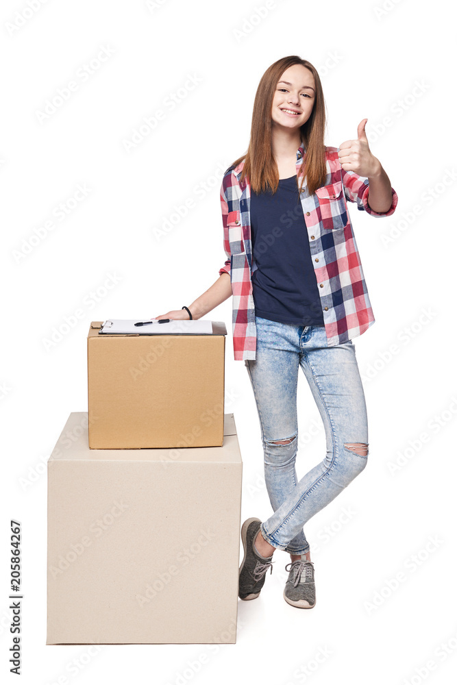Delivery, relocation and unpacking. Smiling young female standing in full length with cardboard boxes gesturing thumb up, isolated on white background Delivery, relocation and unpacking. Smiling young female standing in full length with cardboard boxes gesturing thumb up, isolated on white background