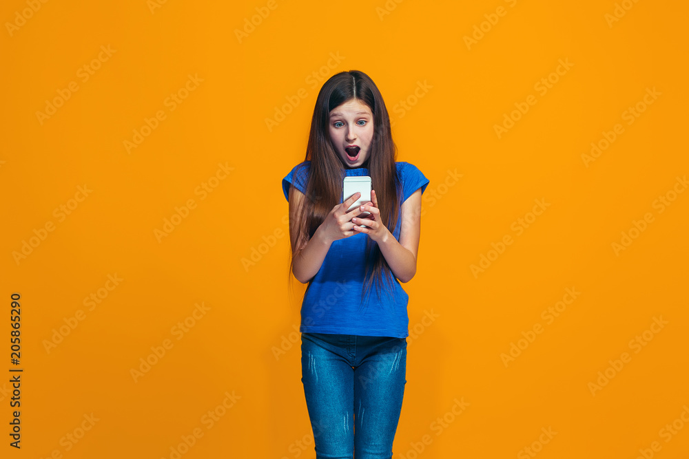 The happy teen girl standing and smiling against orange background. The happy teen girl standing and smiling against orange background.