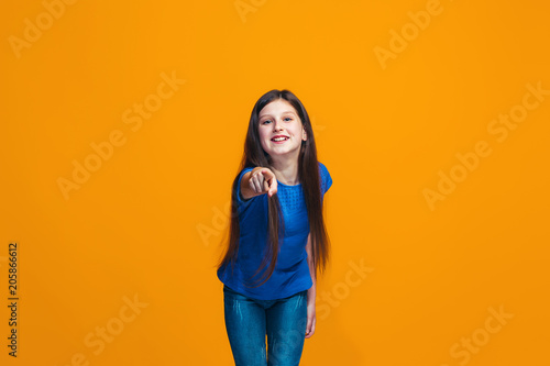 The happy teen girl pointing to you, half length closeup portrait on orange background. © master1305